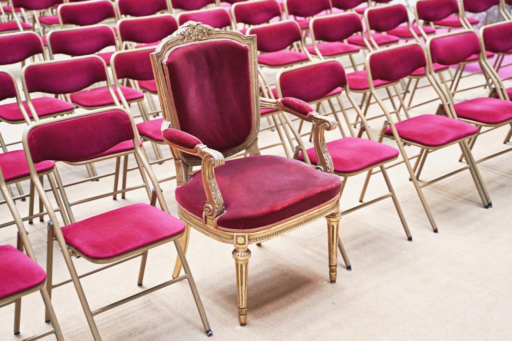 Unique throne or ceremonial armchair with velvet seat and golden details among many simple identical similar chairs. Uniqueness or exclusivity concept. - Eight by Eight